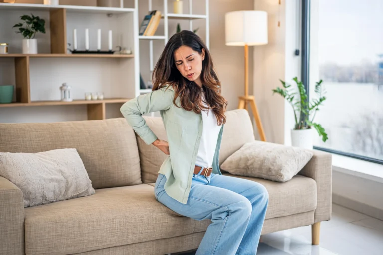 Person experiencing recurring lower back discomfort while sitting at home